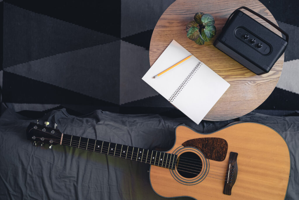 Musical background with acoustic guitar, speaker and notepad on the table, top view. Place for text.